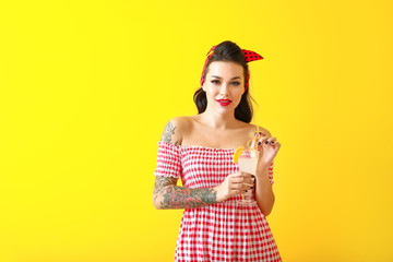 Portrait of beautiful tattooed pin-up woman with cocktail on color background