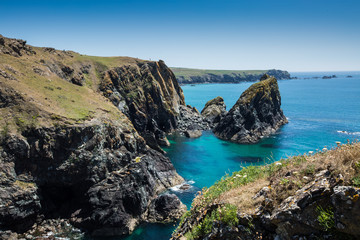 Fototapeta na wymiar A picturesque landscape of Kynance Cove in Cornwall with rugged cliffs over looking a clear blue ocean in summer sunshine