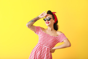 Portrait of beautiful tattooed pin-up woman on color background