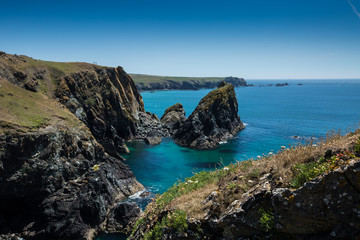 Fototapeta na wymiar A picturesque landscape of Kynance Cove in Cornwall with rugged cliffs over looking a clear blue ocean in summer sunshine