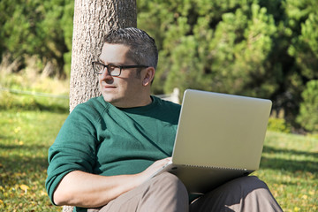 Fototapeta premium Businessman dressing a green sweeter doing his work in a nice park