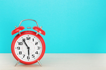 Red retro alarm clock with five minutes to six o'clock, on wooden table on a blue background. The concept of time, holiday, 5 minutes to the event, deadline. Layout with copy space for your text.
