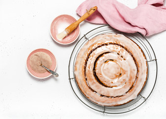 Homemade delicious cinnamon roll cake with sugar icing over white stone background. Copy scape. Top view. 