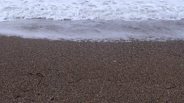Waves slowly rush onto the yellow sand of the beach. Low angle.