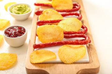 Tasty potato chips, smoked sausages and sauces on light background
