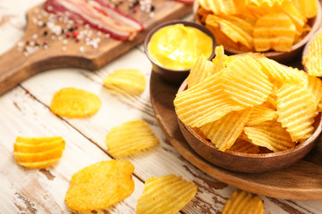 Tasty potato chips and bacon on light wooden background