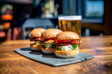 Three Slider Burgers with Tomato Slice, Lettuce, Meat and Cheese and Beer Lager in Background