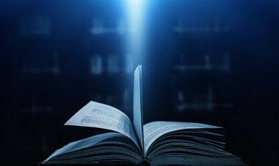 Open book on wooden vintage table with mystic magic bright light on background 