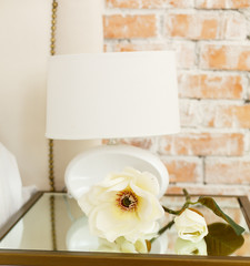 Modern lamp on a glass bedside table. A room in light loft stile with brick wall and light furniture. Comfortable bedroom. A combination of modern and old. Join the glass and brick