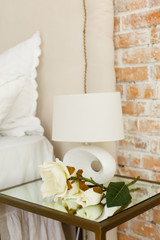 Modern lamp on a glass bedside table. A room in light loft stile with brick wall and light furniture. Comfortable bedroom. A combination of modern and old. Join the glass and brick
