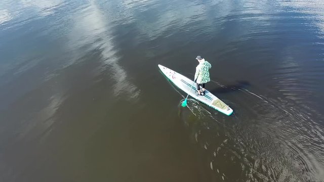 Aerial view of young person in jacket training on a SUP board on a river in sunny day. Footage. Concept of water tourism, healthy lifestyle and recreation