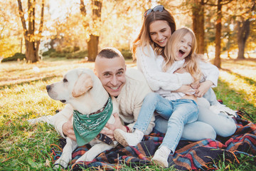 Fototapeta premium Happy beautiful family with dog labrador is having fun are sitting on green grass in park.