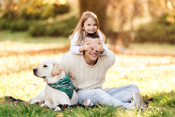 Happy father and daughter with dog labrador is having fun are sitting on green grass in park.