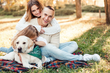 Fototapeta premium Happy beautiful family with dog labrador is having fun are sitting on green grass in park.