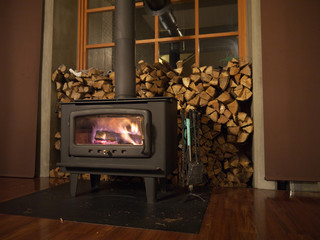 Wood burning stove with glowing coals and logs with stack of knitted firewood in background as symbol of comfort at home