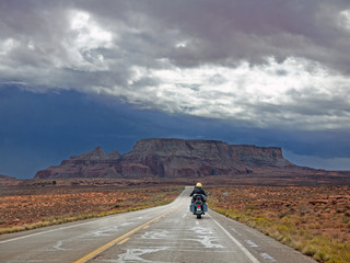 Biker riding on lonely Arizona desert road, red rocks ahead