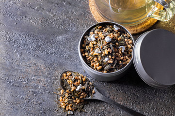Organic and natural brown rice tea, genmaicha in a container. Accompanied by a cup of hot tea on gray background.