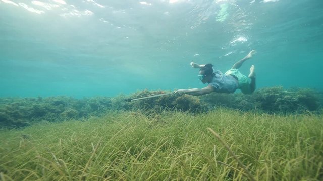 Young man fish hunter shooting fish underwater using a wooden speargun.