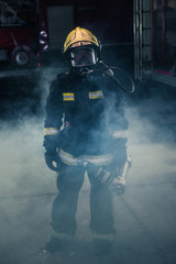 Portrait of a female firefighter wearing a helmet and all safety equipment a while holding a...
