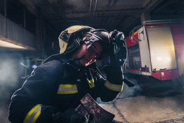 Portrait of a female firefighter while holding an axe and wearing an oxygen mask indoors surrounded by smoke.