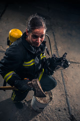 Portrait of a female firefighter while holding an axe and wearing an oxygen mask indoors surrounded by smoke.