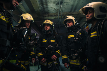 Fototapeta premium Team of firefighters standing inside ( indoors ) a buliding next to a fire engine.
