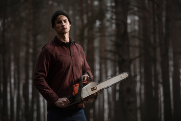 Lumberman working with chainsaw in the forest. Strong lumberjack with the chainsow in the forest.Stylish lumberman getting ready for work. Lifestyle.