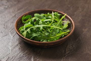 Clay bowl with fresh arugula on a dark stone background. Healthy plant-based diet.