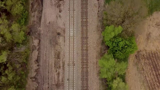 Aerial flyover flying down a railroad track with foliage and field on along the edges on a dreary day.
