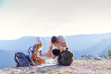 A couple checking their position on the map and enjoying the peak of the mountain, cliff at sunset.