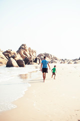 happy family on beach playing, father with son walking sea coast, rocks behind smiling taking vacation