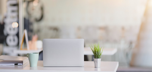 Cropped shot of comfortable workplace with laptop computer and office supplies with sunlight background