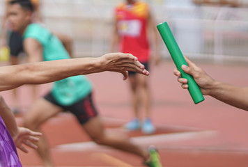 Professional Athlete passing a baton to the partner against race on racetrack.selective focus. - obrazy, fototapety, plakaty