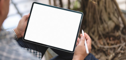Close-up view of young male freelancer working on his project with blank screen tablet with garden...