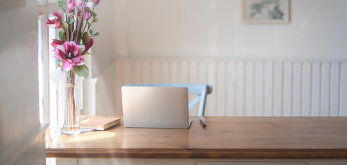 Close-up view of comfortable workplace with mock up laptop computer, office supplies and pink flower vase on wooden table