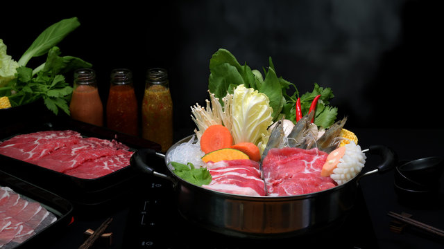 Close-up view of shabu shabu in hot pot with black background, fresh sliced meat, sea food and vegetables
