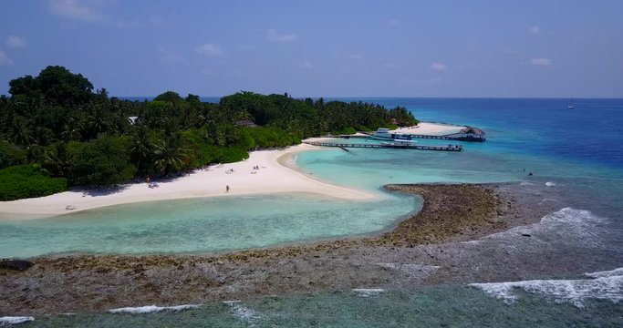 Large rocky barrier and coral reef around calm tranquil water washing white sand beach on bay of tropical island with harbor and piers in the Maldives