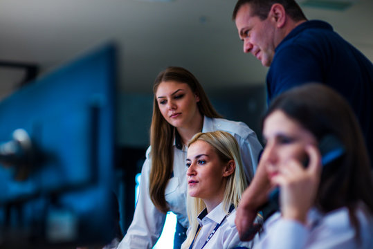 Security Guards Working In Surveillance Room. Female Security Guard With Portable Transmitter Monitoring Cameras Indoors At Night.