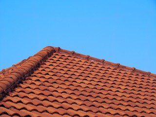 Roof covered with orange wavy tiles with blue sky background.