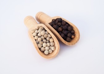 White pepper and black pepercorn in wooden scoop isolated on white background.