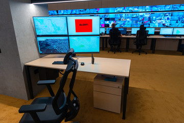 Close up photo of a walkie-talkie on an empty desk in front of a monitor at the main security data cyber center.