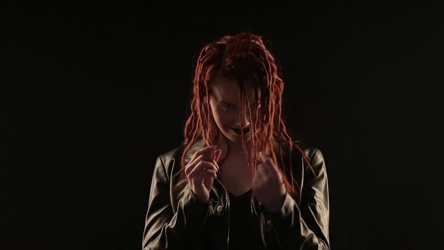 concept dances, parties, advertising leather jackets, styling hair, hairdressing dreadlocks, make-up: dark lipstick. rocker dancing on black background, woman styling red hair