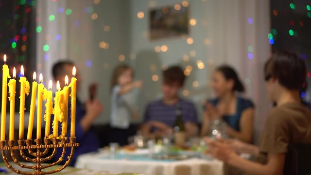 Jewish family celebrates Hanukkah. Festive dinner with traditional food. Lighting the menorah lights