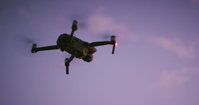 A silhouette of a quadcopter drone flying in the sky at dusk with purple pink clouds