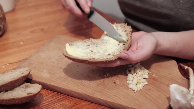 Woman's hands butter a slice of bread, the chopped garlic lies on a chopping board. Preparations for making a sandwich with garlic. Close Up.