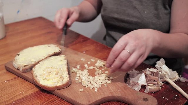 Woman's hands puts garlic on a slice of bread spread with butter. Preparations for making a sandwich with garlic.