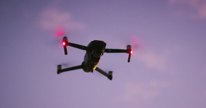A silhouette of UAV drone flying with red signal lights in the sky at dusk with purple pink clouds
