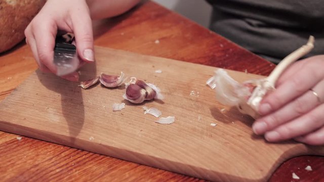 Woman's hands peeling garlic on a chopping board. Preparations for making a sandwich with garlic. Close up.