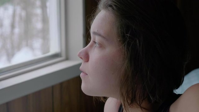 Girl looking snow fall outside through window, slow motion close up