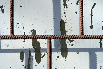 Fragment of an old window painted by white paint behind a rusty brown bars on a sunny day. Abstract background